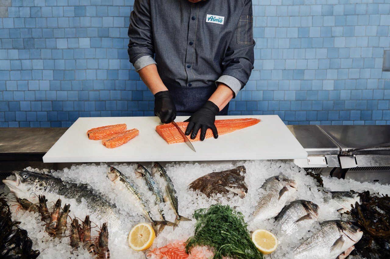 A cook with a jacket that has Valio Aimo logo on it preparing salmon